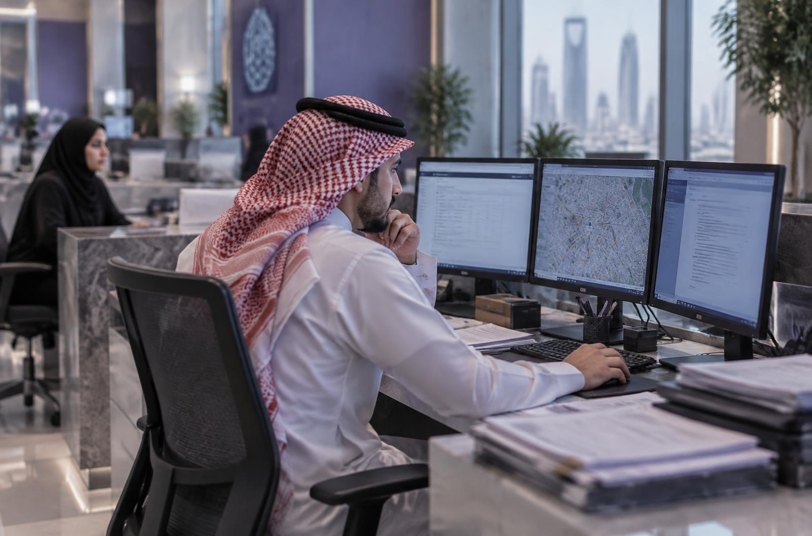 An employee in a Riyadh office working across several separate systems and paper files